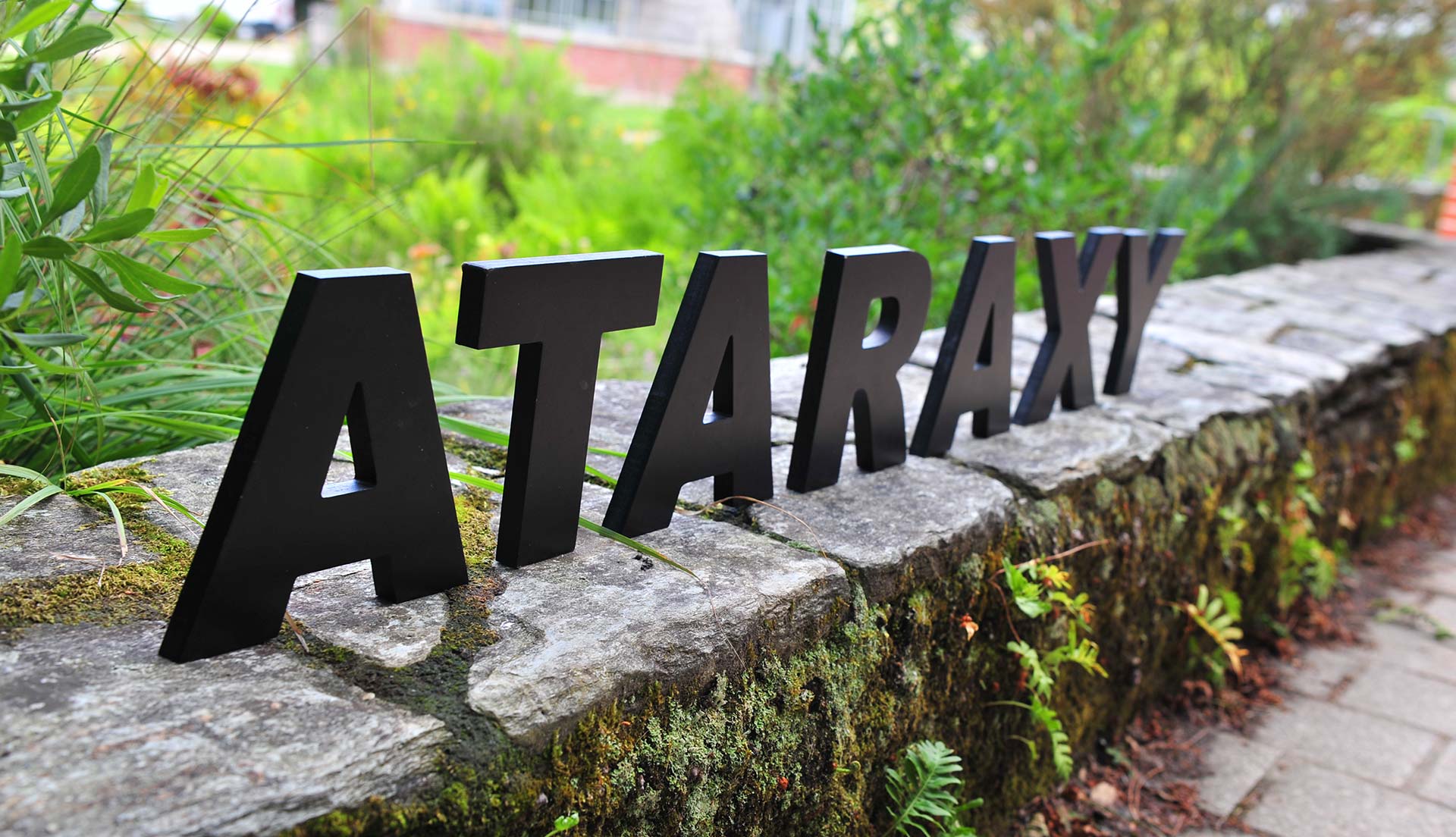 Logo Ataraxy sur un muret de pierre dans un jardin à Nantes